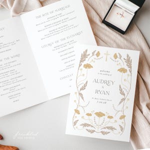 May include: Wedding stationery set featuring a gold ring in a black box, and a program with floral design. The program includes the names Audrey & Ryan, and the date 7.22.28.