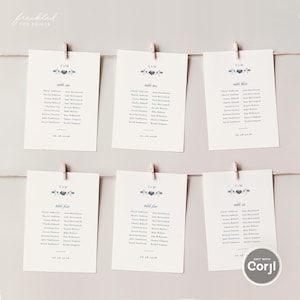 May include: Six wedding table seating cards hanging from a string with wooden clips. Each card has a floral design, the initials "V & M", and a list of names. The date "06.16.2018" is printed at the bottom of each card.