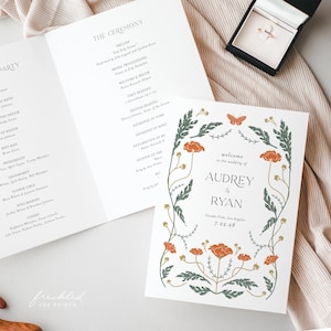 May include: Wedding stationery set featuring a floral design with orange flowers and green leaves. The invitation reads "welcome to the wedding of Audrey & Ryan" with the date and location. A ring box with a gold ring is also visible.