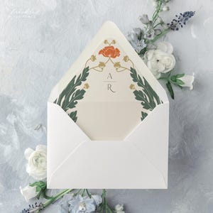May include: A white envelope with a floral design on the front. The design features a red poppy flower, green leaves, and gold accents. The initials "A R" are printed in gold in the centre of the design.