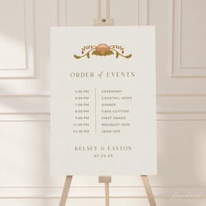 以下が含まれることがあります： 金色の文字と花柄のデザインが施された白いウェディングサイン。サインには、結婚式のリセプションのイベントの順番が記載されており、セレモニー、カクテルアワー、ディナー、ケーキカット、ファーストダンス、ブーケトス、送別会などが含まれています。サインには、Kelsey & Eastonの名前と日付07.22.25も記載されています。