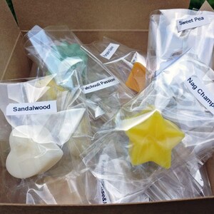 May include: A box filled with small, clear bags containing various scented wax melts. The wax melts are shaped like stars, hearts, and other geometric shapes. The bags are labelled with the scents: Sweet Pea, Nag Champa, Sandalwood, Patchouli Passion, and Frankincense & Myrrh.