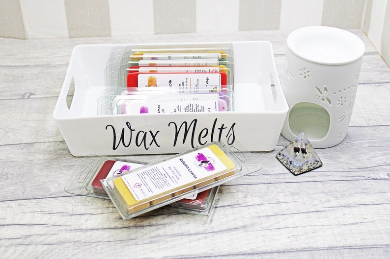 May include: A white ceramic wax warmer with a floral design, a white tray labeled "Wax Melts" filled with various wax melts, and a clear glass pyramid with a blue and white design.