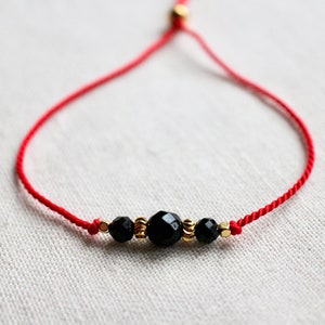 May include: A red string bracelet with three black faceted beads and gold accents.