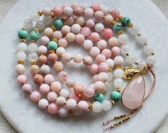 Pode incluir: Um colar mala de pedras preciosas rosa, branco e turquesa com um pingente de quartzo rosa. O colar é feito de pedras naturais e apresenta um detalhe dourado.