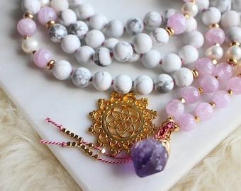 Pode incluir: Um colar mala de várias voltas com contas de howlite branca, quartzo rosa e pérolas. O colar tem um pingente dourado com um design de flor da vida e um cristal de ametista roxo.