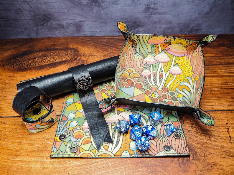 May include: A set of dice rolling trays and a dice rolling tower, all with a colorful mushroom and floral pattern. The trays are made of leather and have a black strap. The tower is made of leather and has a metal D20 charm. The dice are blue and have white numbers.