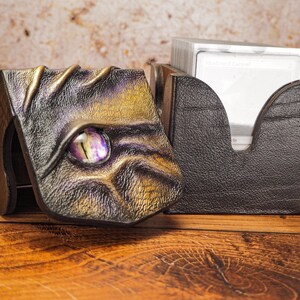 May include: A black leather card box with a dragon design. The box has a purple gem eye and gold accents. The box is open and a stack of cards is visible inside.