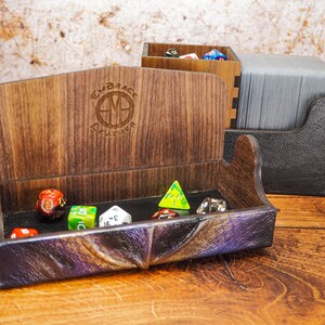 May include: A wooden dice tray with a leather-like lining and a compartment for cards. The tray is filled with colorful dice and has the text "Embrace the Adventure" engraved on the side.