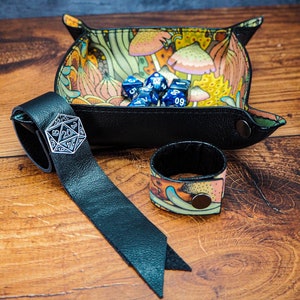 May include: A black leather dice tray with a colorful mushroom design. The tray is filled with blue dice. A black leather dice bag with a silver metal dice charm is also pictured.