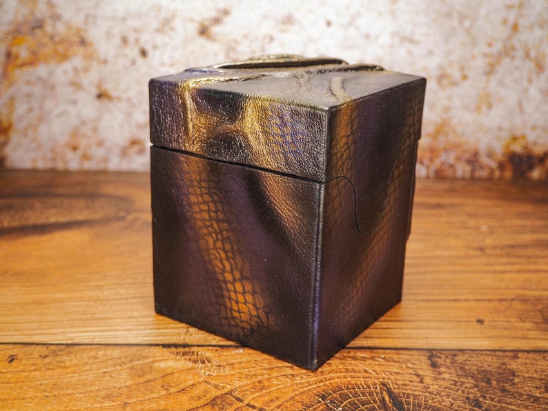 May include: A small, square box with a textured, black and gold finish. The box has a unique, almost scaly, pattern.