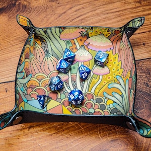May include: A blue and black dice tray with a colorful mushroom and floral pattern. The tray is filled with blue dice with white numbers.