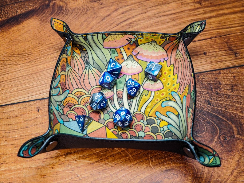 May include: A blue and black dice tray with a colorful mushroom and floral pattern. The tray is filled with blue dice with white numbers.