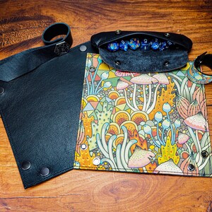 May include: A black leather dice tray with a colorful mushroom and geometric pattern. The tray has a separate compartment for dice, which is lined with black felt. The tray has a black leather wrist strap with a metal buckle.