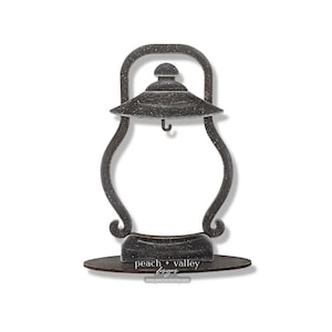 May include: A black metal lantern-shaped picture frame with a distressed finish. The frame has a hook on the top and sits on a wooden base with the text "peach + valley designs" and a website address.