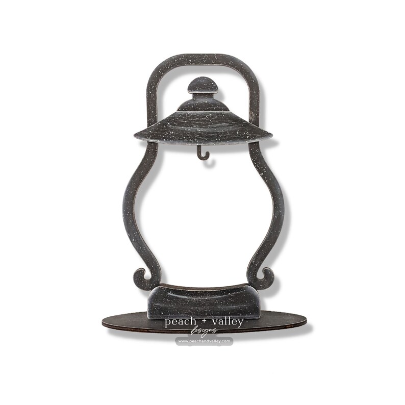 May include: A black metal lantern-shaped picture frame with a distressed finish. The frame has a hook on the top and sits on a wooden base with the text "peach + valley designs" and a website address.