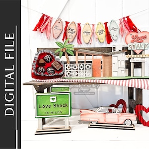 May include: A Valentine's Day themed craft kit featuring a red heart-shaped box with chocolates, a wooden sign that says "Love Shack 15 Miles", a pink car, and a wooden sign that says "Love Shack" with a red heart and the words "Stay Away Fools".