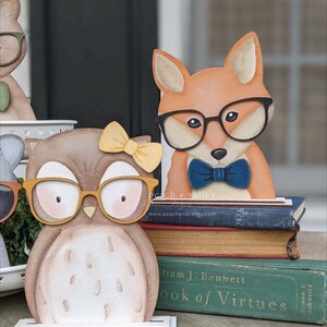 May include: A wooden owl and fox figurine with glasses and a bow tie. The figurines are standing on a stack of books with the title "Book of Virtues".