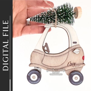 May include: A wooden car ornament with a small artificial Christmas tree on top. The car is painted white and brown and has a red dot on the back. The car has the text "Navy 2021" on the side.