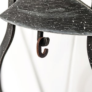 May include: A black wooden shelf with a distressed white paint finish. The shelf has a small wooden hook attached to the bottom. The text "peach valley" is visible on the shelf.