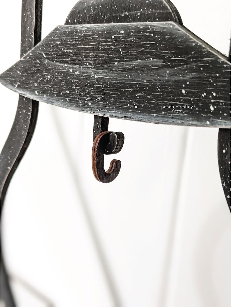 May include: A black wooden shelf with a distressed white paint finish. The shelf has a small wooden hook attached to the bottom. The text "peach valley" is visible on the shelf.