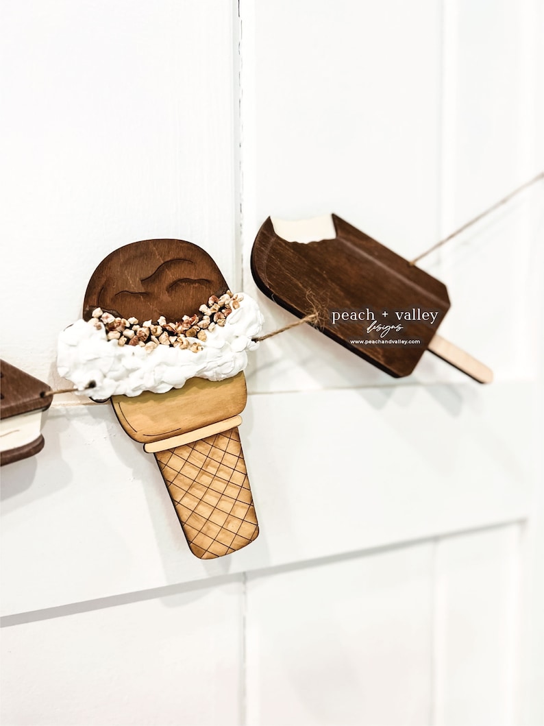 May include: Wooden ice cream cone and popsicle cutouts with a white background. The ice cream cone has a brown scoop of ice cream with white frosting and brown sprinkles. The popsicle is brown with a white bite taken out of the top. The text "peach + valley designs" is printed on the popsicle.