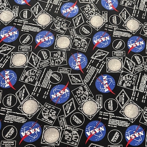 May include: Black fabric with a repeating pattern of white and blue NASA logos, white outlines of the moon, and white text that reads "Exploring, Innovating, Inspiring".