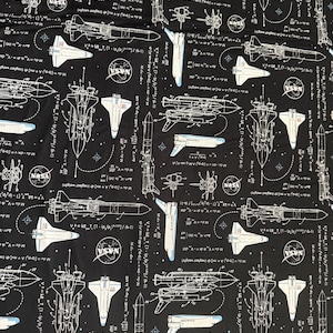 Może przedstawiać: Czarny materiał z powtarzającym się białym wzorem przedstawiającym wahadłowce kosmiczne, rakiety i wzory naukowe. Tekst zawiera logo NASA i równania.