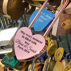 May include: A pink heart-shaped padlock with the inscription "May every moment be filled with love Brian & Sarah Paris 2019" attached to a collection of other padlocks.