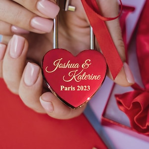 May include: A red heart-shaped padlock with the inscription "Joshua & Katerine Paris 2023" in gold lettering.