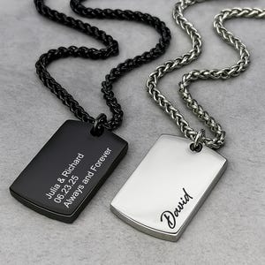May include: Two dog tag necklaces. One is black with the inscription "Julia & Richard 06.23.25 Always and Forever." The other is silver with the name "David." Both tags hang from a chain.