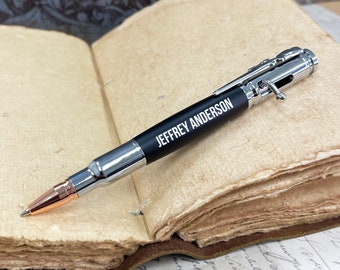 May include: A black and silver bullet pen with a personalized inscription that reads "JEFFREY ANDERSON". The pen is lying on a closed book with aged pages.