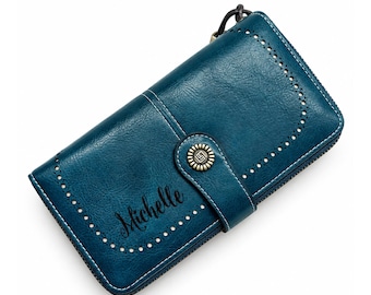 May include: A teal rectangular wallet featuring a snap-button closure with a metallic emblem, a decorative perforated border, and the name Michelle embossed in black script on the front surface. The wallet includes a side zipper pull.