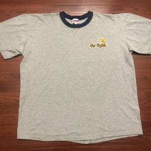 May include: Gray t-shirt with a blue and white ringer neck. The shirt has a yellow and blue West Virginia logo on the front.