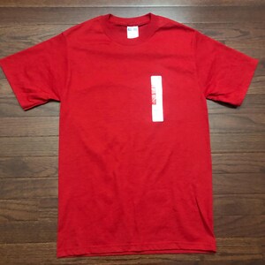 May include: A plain red t-shirt with a white tag on the front.