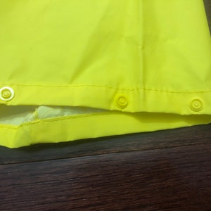 May include: Close-up of the bottom edge of a bright yellow raincoat with three white snap buttons.