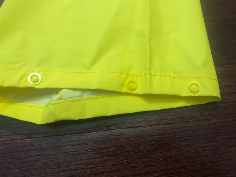 May include: Close-up of the bottom edge of a bright yellow raincoat with three white snap buttons.