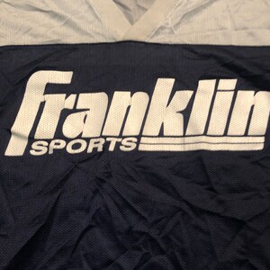 May include: A navy blue and white athletic jersey with the text "Franklin Sports" in white.