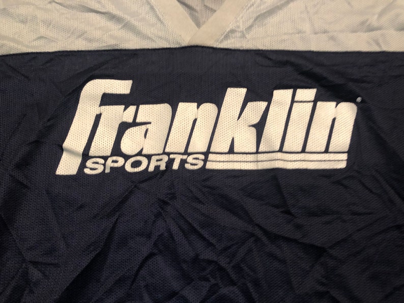 May include: A navy blue and white athletic jersey with the text "Franklin Sports" in white.