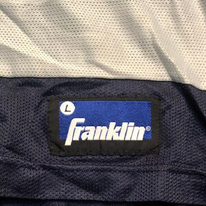 May include: A blue and white athletic jersey with a navy blue label that reads "Franklin" with a size "L" in a white circle.