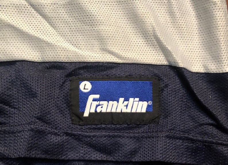 May include: A blue and white athletic jersey with a navy blue label that reads "Franklin" with a size "L" in a white circle.