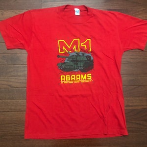 May include: Red t-shirt with a graphic of a green M1 Abrams tank with the text "M1 Abrams U.S. Army Armor Center - Fort Knox, KY"