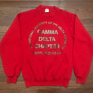 May include: Red sweatshirt with a gold circle graphic that reads "The National Sorority of Phi Delta Kappa, Inc. Gamma Delta Chapter, Flint, Michigan."
