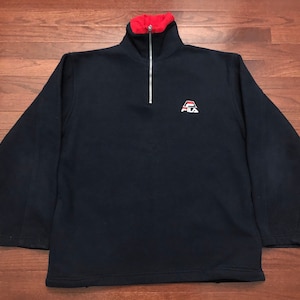 May include: A navy blue fleece pullover with a quarter zip closure. The collar is lined with red fabric. The pullover features a white Fila logo with red and blue accents.