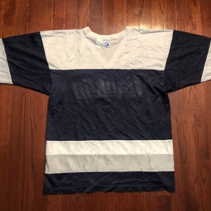 May include: A navy blue and white striped t-shirt with a large white logo on the front. The logo is a stylized word that is difficult to read.