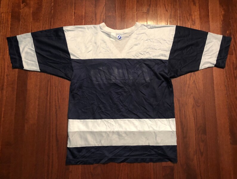 May include: A navy blue and white striped t-shirt with a large white logo on the front. The logo is a stylized word that is difficult to read.