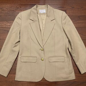 May include: A beige blazer with two gold buttons and two pockets. The blazer has a single-breasted closure and a notched lapel.