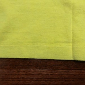 May include: Close-up of the bottom edge of a bright yellow t-shirt. The fabric is smooth and the stitching is visible.