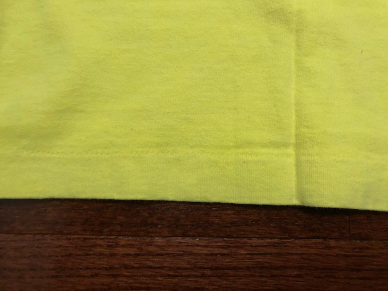 May include: Close-up of the bottom edge of a bright yellow t-shirt. The fabric is smooth and the stitching is visible.