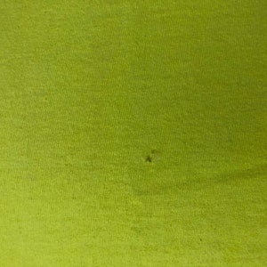 May include: A close-up of a bright green fabric with a subtle texture. The fabric has a small hole in the center.
